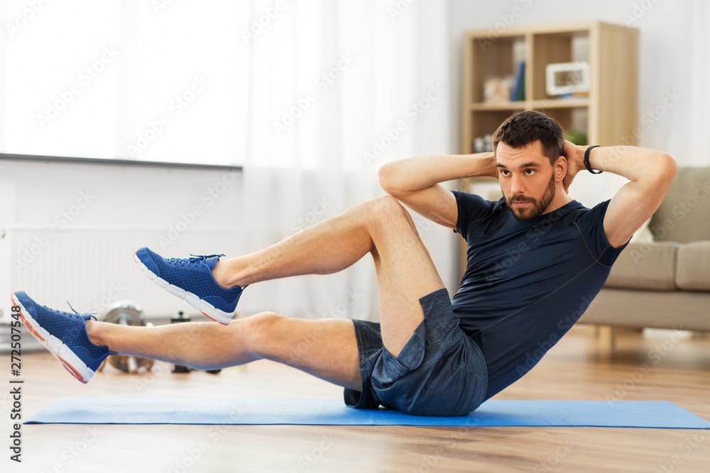 sport, fitness and healthy lifestyle concept - man making bicycle crunch on exercise mat and flexing abs at home